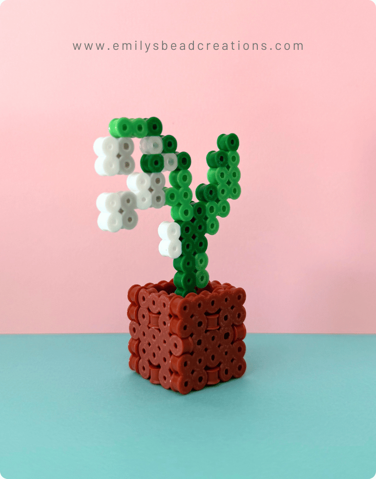 A photo of a lily of the valley Perler bead 3D potted flower, with a blue and pink background. 