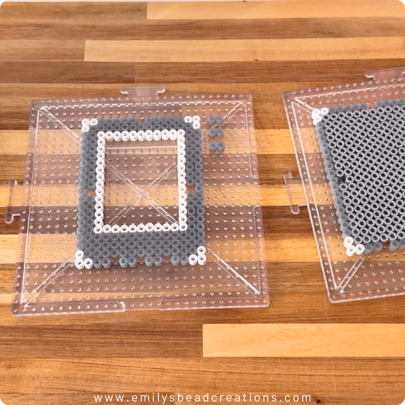 Large square pegboards with silver and white Perler beads in the shape of an instant photo frame. The photo features a wood background and 1.5 pegboards with beads.
